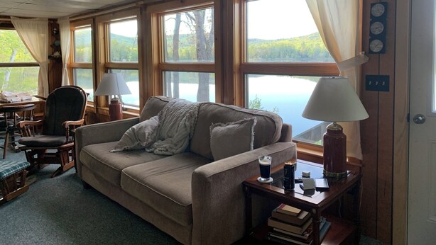 Un salon chaleureux avec un canapé beige, une table basse en bois et une vue sur un lac, visible à travers de grandes fenêtres.