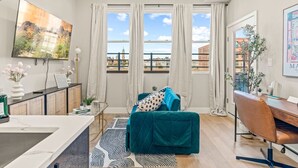 Een moderne woonkamer met een turquoise bank, een eethoek met een houten tafel, en een keuken met een wit aanrecht.