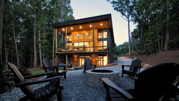 Une cabane moderne avec un foyer et des fauteuils Adirondack, située dans un cadre forestier.