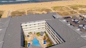 An aerial view of a hotel with a swimming pool, beach access, and a parking lot.