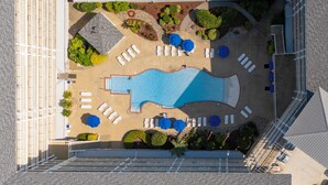 An aerial view of a hotel pool area with sun loungers, a swimming pool, and landscaped garden beds.