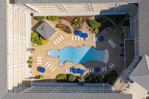 An aerial view of a hotel pool area with sun loungers, a swimming pool, and landscaped garden beds.