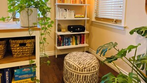 A cozy reading nook with a bookshelf, a potted plant, and a patterned ottoman. - Charming and Spacious 2B + 2.5 Bath Townhome (Pasadena)