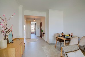A modern dining area with a wooden table set for four, a vase with flowers, and a view into the kitchen.