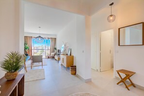 A spacious living area with a sofa, chairs, a coffee table, and a dining table. There is a large window providing a view of the outside.