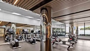 A gym with various exercise equipment, a large mirror, and a modern ceiling design. - Luxury Sky High Apartment with Pool Gym & Parking (South Melbourne)