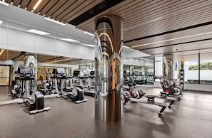 Ett gym med olika typer av träningsredskap, en stor spegel och en modern takdesign.