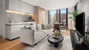 A modern apartment with a kitchen, living area, dining space, and a large window with a city view. - Luxury Sky High Apartment with Pool Gym & Parking (South Melbourne)