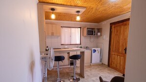 Une cuisine avec des meubles de rangement en bois, un four à micro-ondes, un évier et deux tabourets de bar.
