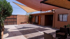 Un espace patio doté d’un sol en pierre, de mobilier d’extérieur et d’une grande voile d’ombrage.