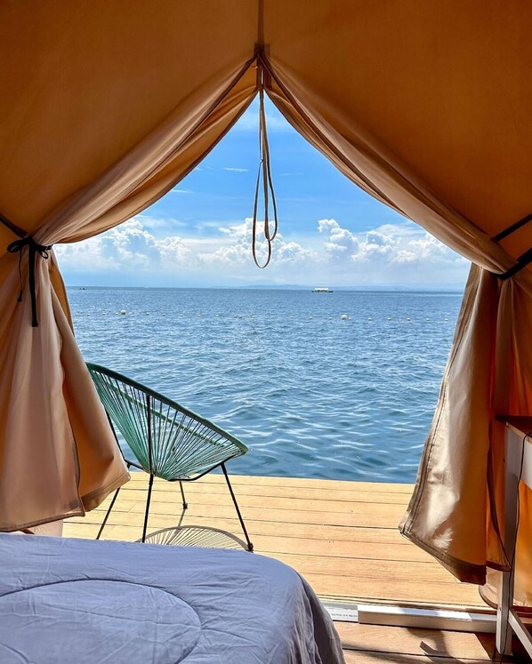A tent with a view of the sea, a chair, and a bed.