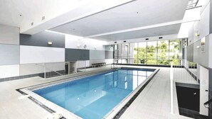 An indoor swimming pool with a tiled floor, a metal ladder, and a view of greenery outside. - Executive Apartment - Great Location Close to Attractions, Shops & Eateries (Wellington)