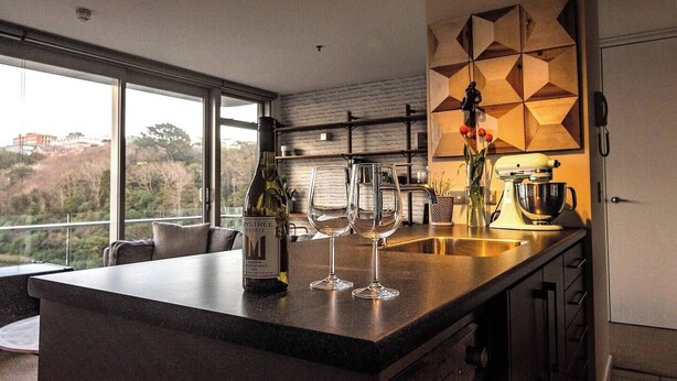 A modern kitchen with a large island, wine glasses, a bottle of wine, and a mixer. - Executive Apartment - Great Location Close to Attractions, Shops & Eateries (Wellington)
