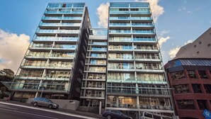 A modern high-rise building with multiple floors, large windows, and a prominent entrance area. - Executive Apartment - Great Location Close to Attractions, Shops & Eateries (Wellington)