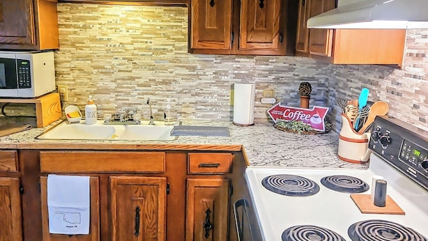 A kitchen with wooden cabinets, a microwave, a stove, and a stone backsplash.