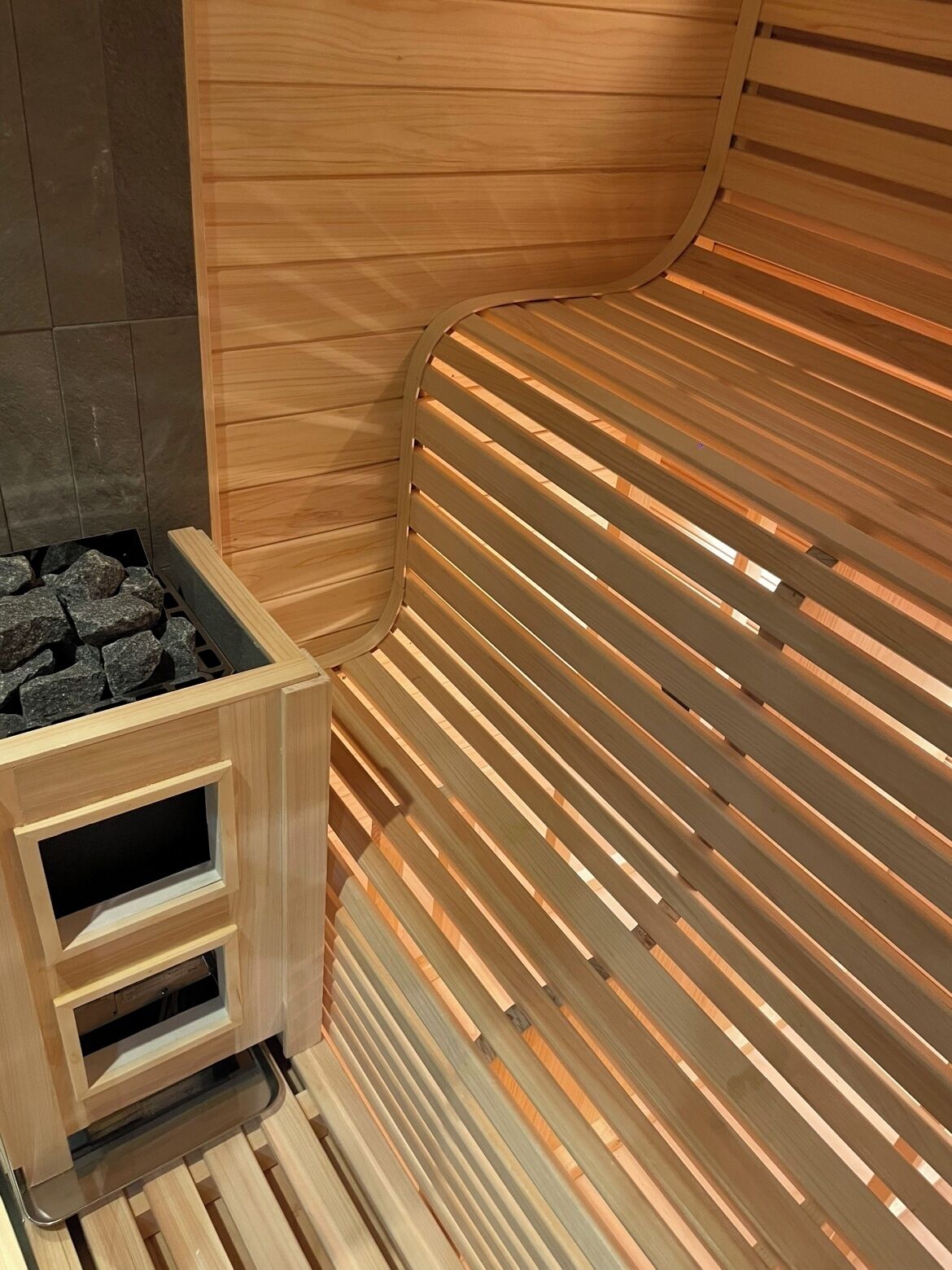 Una sauna con un banco de madera y un elemento calefactor de piedra.