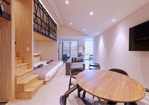 A modern hotel room with a wooden staircase, a sofa, a dining table, and a view of the outside through large windows. - Sakura Cross Inn & Sauna Ishigaki (Ishigaki)