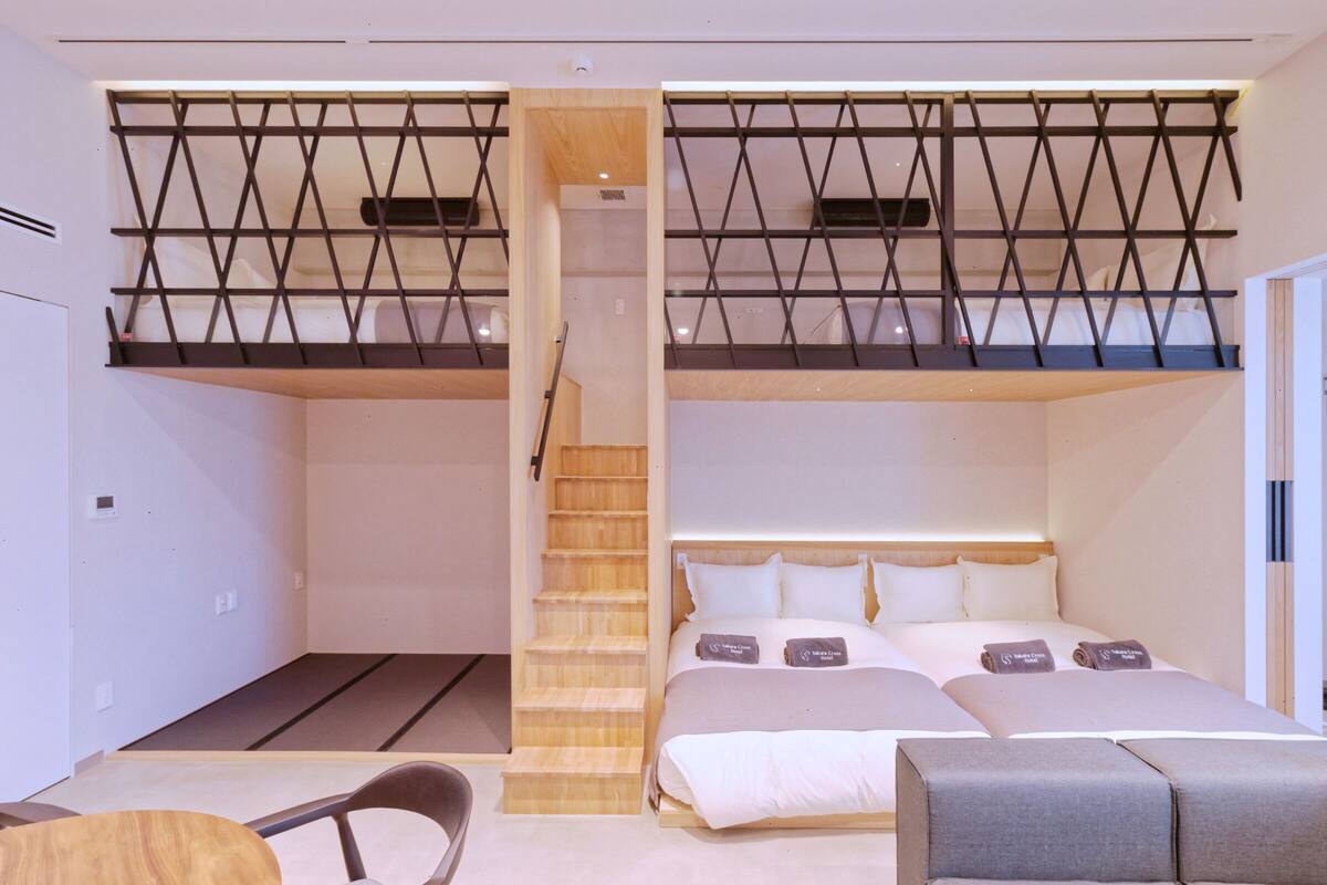 Una habitación de hotel moderna con una zona de dormir en altura, una escalera de madera y un área de descanso con una mesa y sillas.