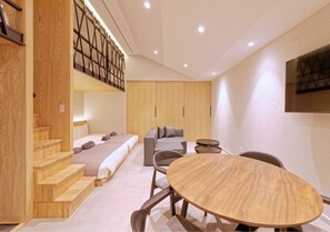 A modern hotel room with a wooden staircase, a sofa, a dining table, and a view of the city. - Sakura Cross Inn & Sauna Ishigaki (Ishigaki)