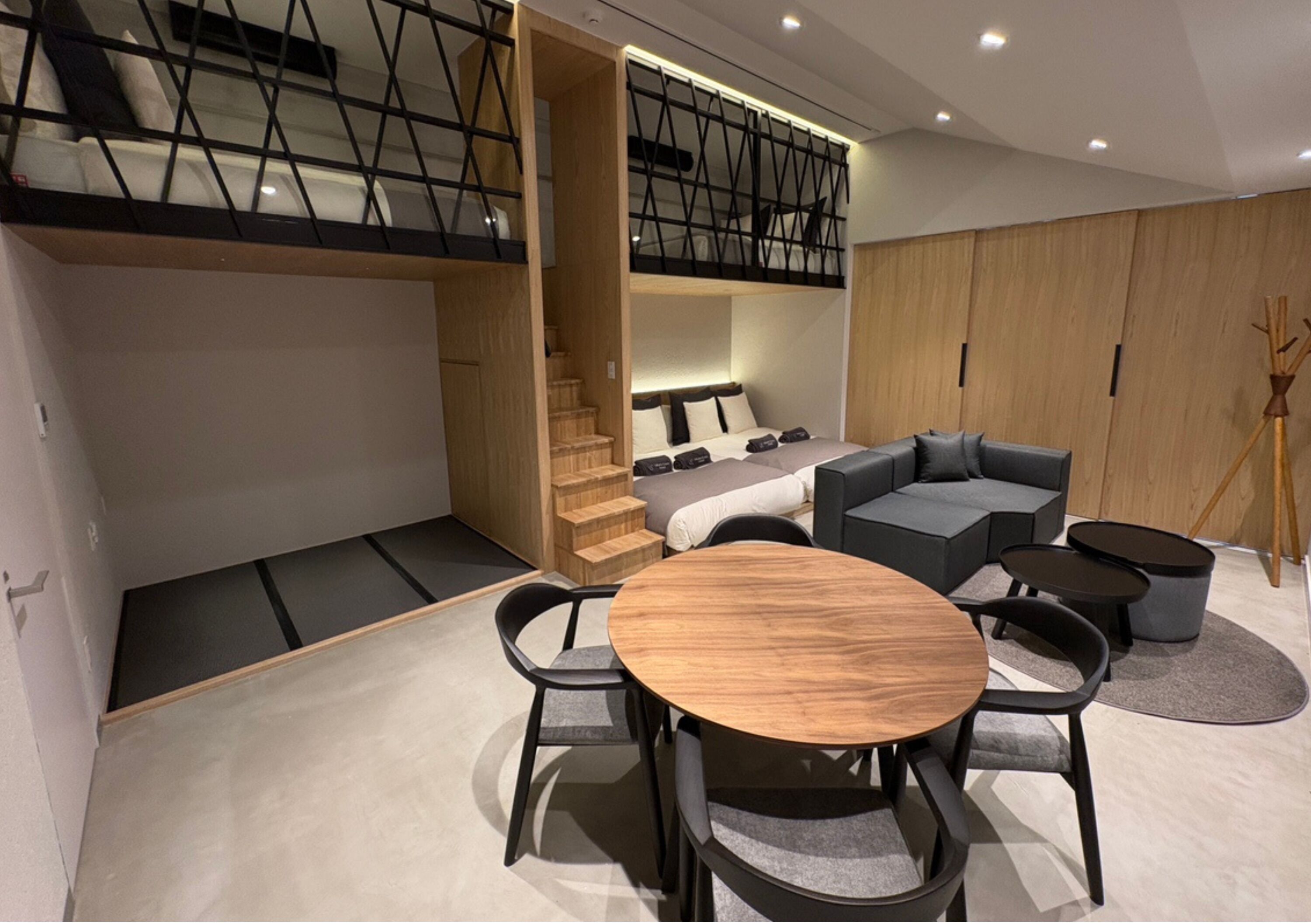 Una habitación compacta y moderna con cama altillo, sofá, mesa de comedor y una pequeña escalera.