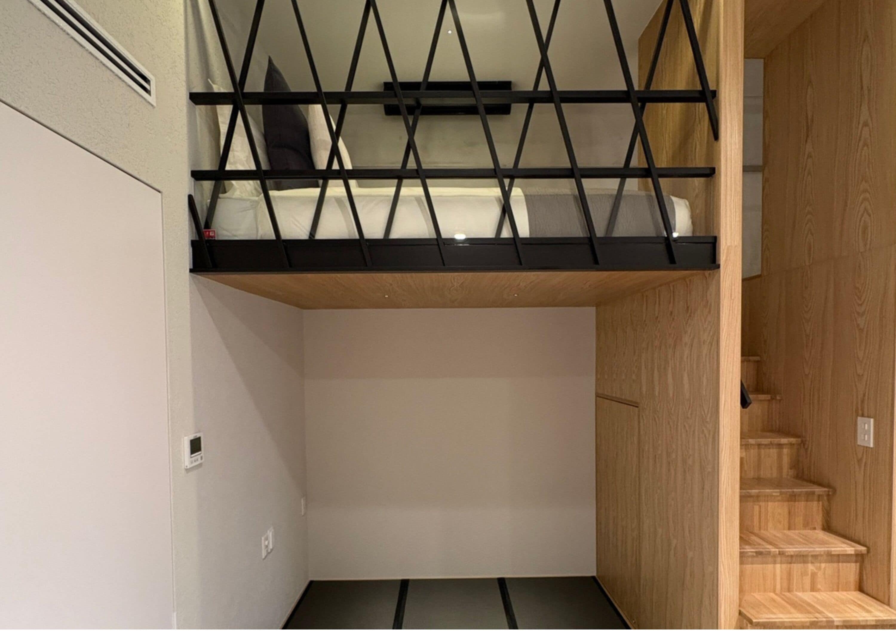 A bunk bed with a wooden ladder, a white wall, and a wooden staircase.