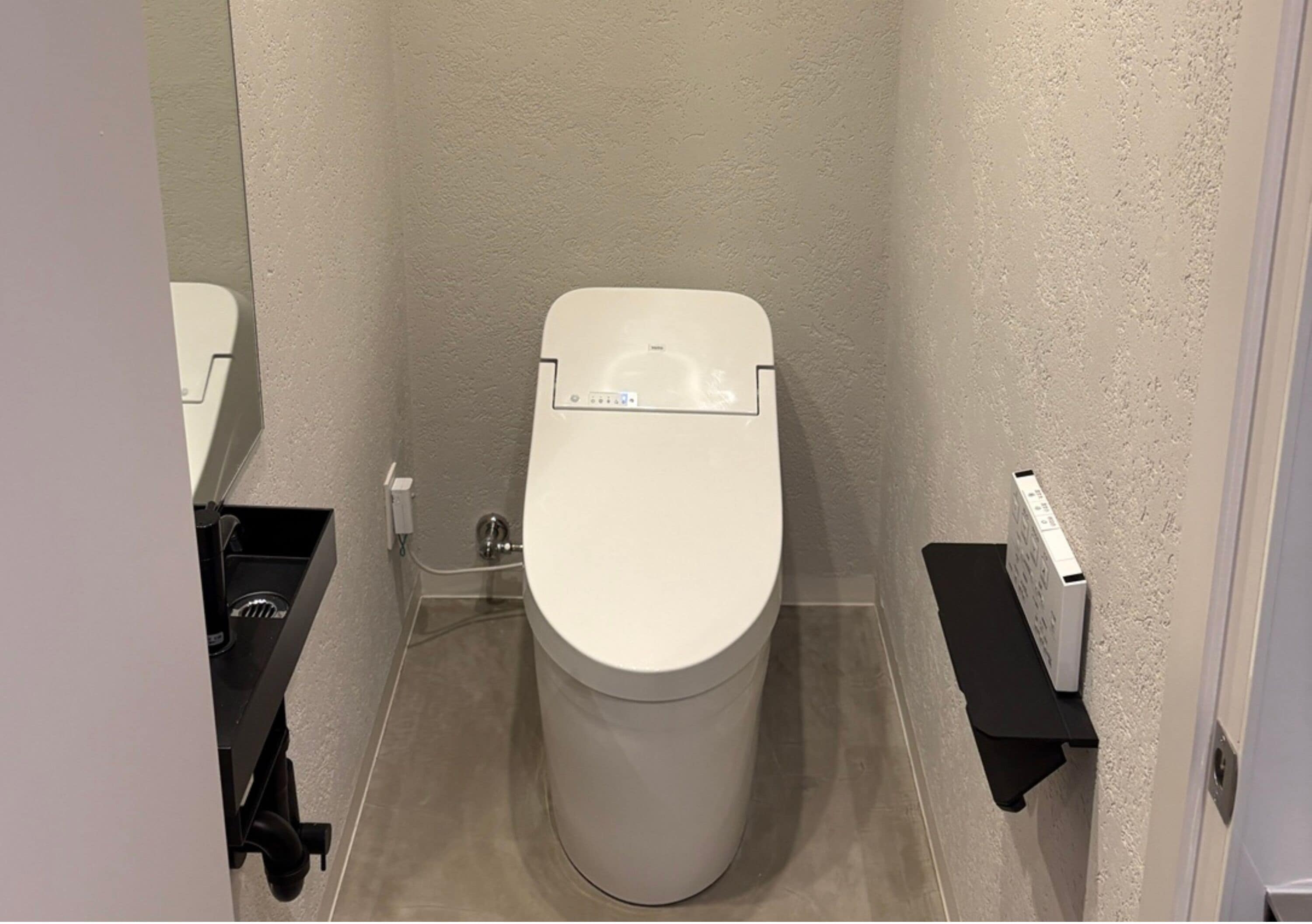 A compact bathroom with a white toilet, a small shelf, and a visible pipe.