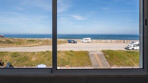 Blick auf einen Strand durch ein Fenster, mit geparkten Fahrzeugen und blauem Himmel.