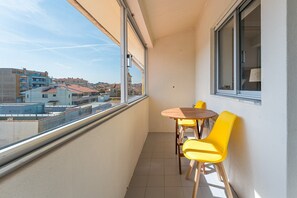 Un balcon donnant sur des immeubles, une table et des chaises jaunes.
