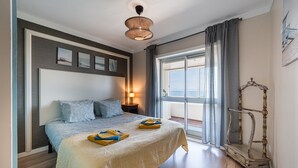 Ein Schlafzimmer mit Bett, Nachttisch, Lampe, Meerblick und einem dekorativen Sessel.