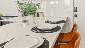 A kitchen with a white marble countertop, a plant, and a dining area with a chair and a table set for four. - Luxury 1BR|1BA in the Heart of Fishtown (Philadelphia)