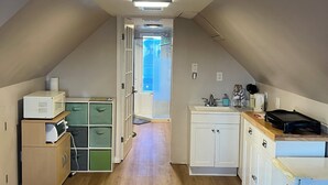 Teto estreito e inclinado, com ventoinha e iluminação embutida. Um corredor leva a uma porta com painel de vidro.