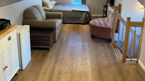 Quarto de sótão acolhedor, com uma cama, dois sofás, uma mesa pequena e um frigorífico.