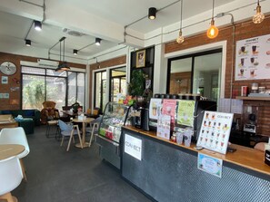 Un interior de cafetería con mostrador, zona de estar y un gran osito de peluche.