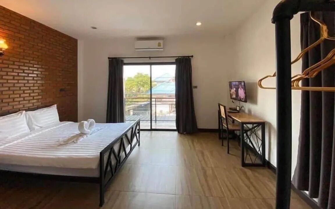 Habitación de hotel con cama, escritorio, televisor y balcón con cortinas.