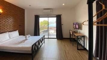Habitación de hotel con cama, escritorio, televisor y balcón con cortinas.