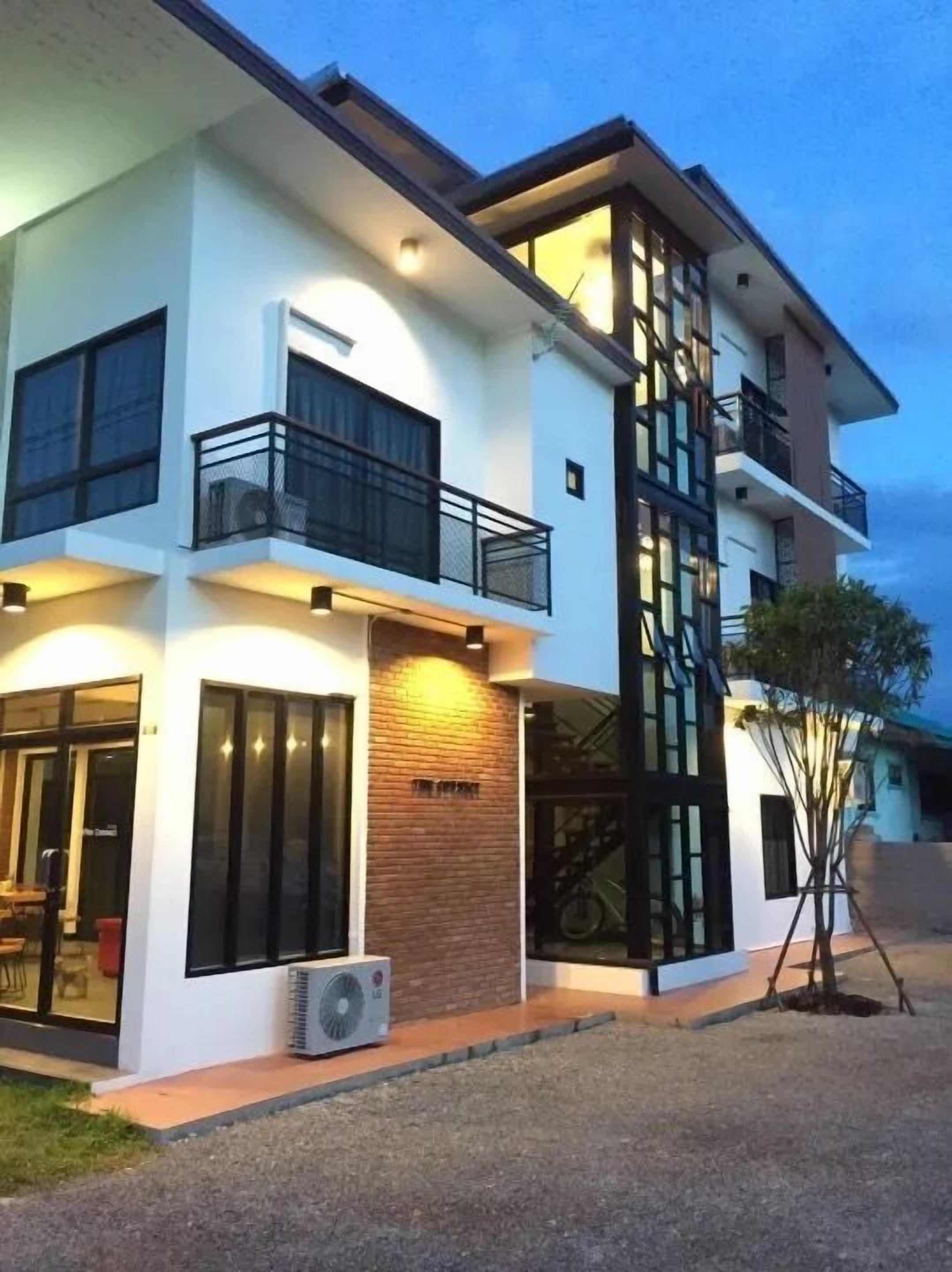 Un edificio moderno de varios pisos con balcones, ventanas amplias y una unidad de aire acondicionado en la planta baja.