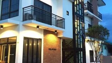 Un edificio moderno de varios pisos con balcones, ventanas amplias y una unidad de aire acondicionado en la planta baja.