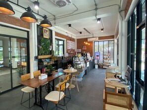 Una cafetería con mesas, sillas, una barra y un amplio ventanal.
