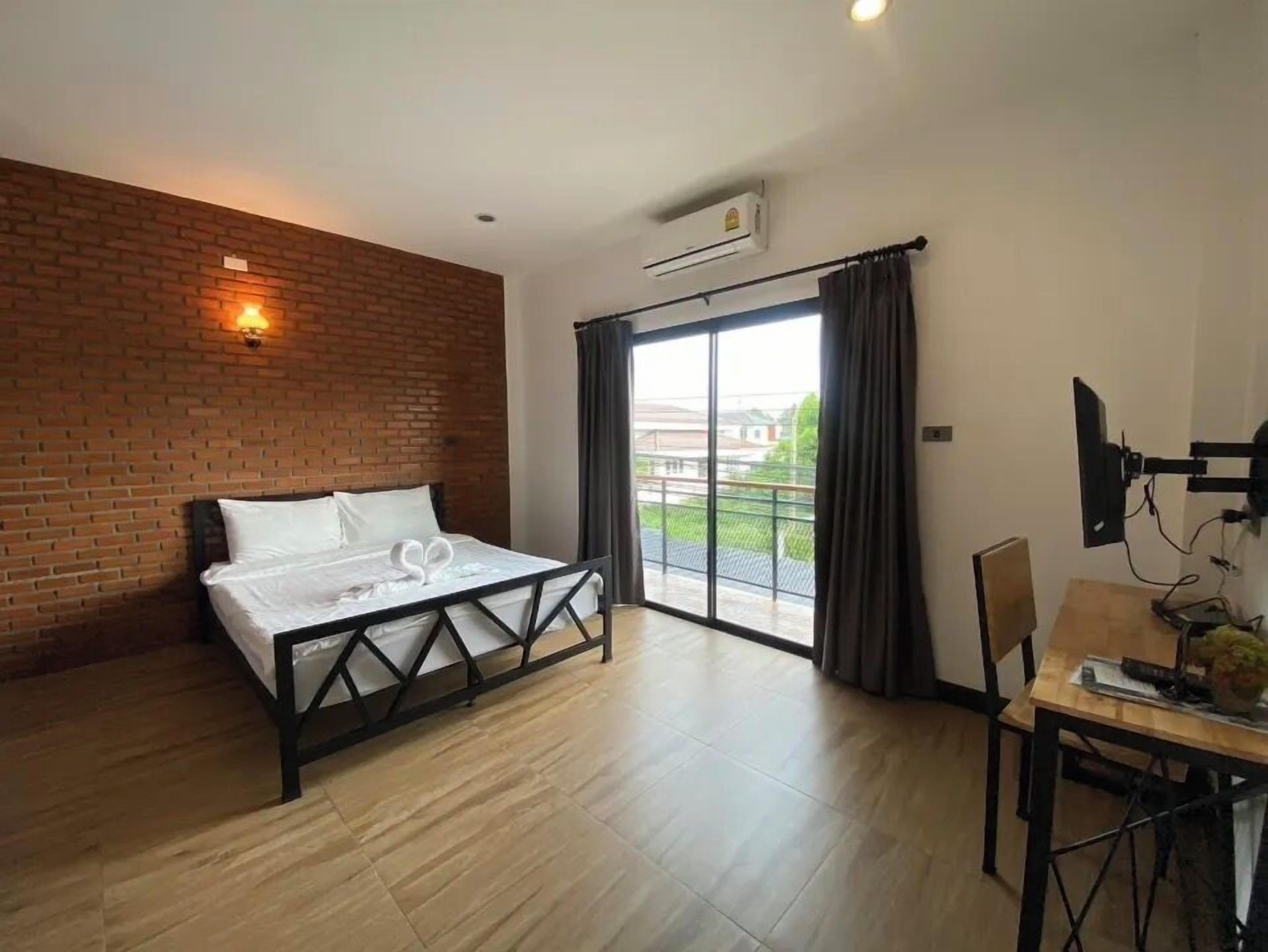 A bedroom with a bed, a desk, a chair, a TV, and a large window with curtains.