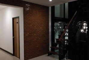 A hallway with a wooden door, a brick wall, and a staircase with metal railings. - The Connect Chiang Mai (Chiang Mai)