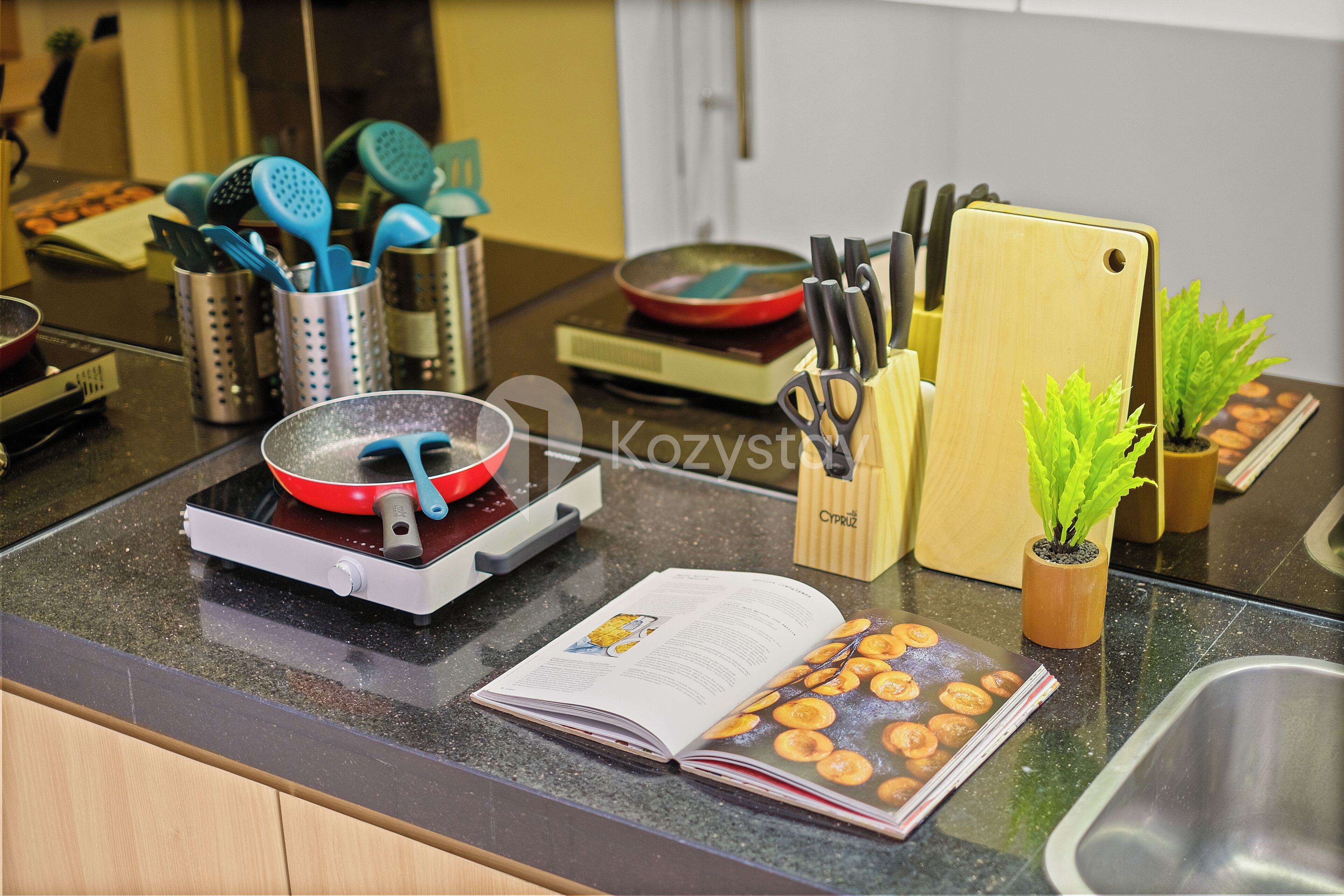 A kitchen counter with a frying pan, a cookbook, and various kitchen utensils.