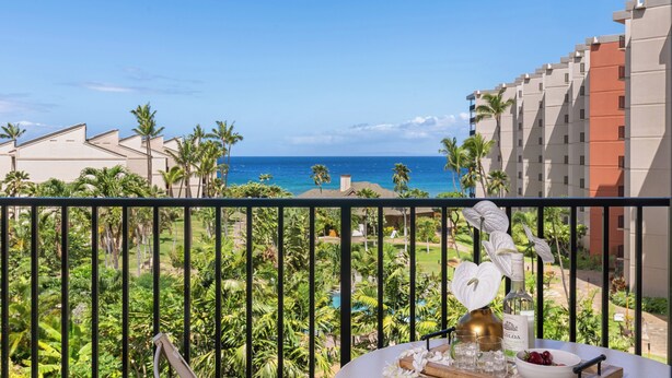 A balcony with a view of the ocean, palm trees, and a pool. - Oceanview 2BD Condo Steps to the Pool - Kaanapali Shores 529 (Lahaina)