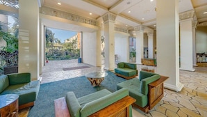 A spacious lobby with green sofas, a central coffee table, and a view of an outdoor garden area. - Oceanview 2BD Condo Steps to the Pool - Kaanapali Shores 529 (Lahaina)