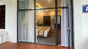 A hotel room with a large sliding glass door, a bed with a headboard, a nightstand, and a mirror. - Him Lam Eco Resort (Dien Bien Phu)