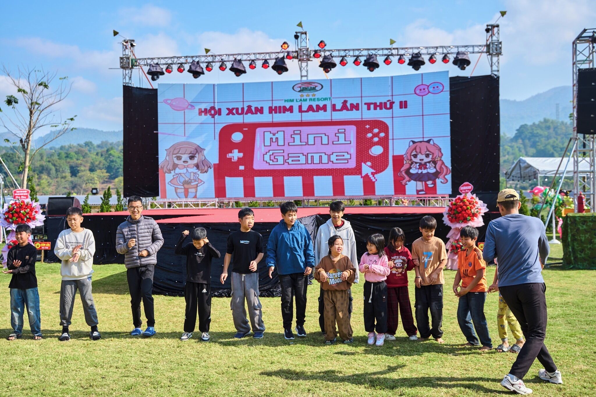 Un grupo de personas de pie frente a un escenario con una gran pantalla mostrando un anuncio de juego.