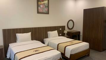A hotel room with two beds, a wooden headboard, a nightstand with a lamp, a wardrobe, and a painting on the wall.