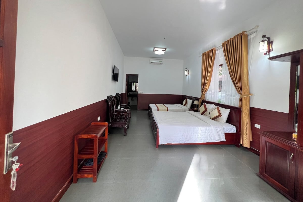 Een hotelkamer met twee bedden, een houten bankje, een kast en een televisie aan de muur.