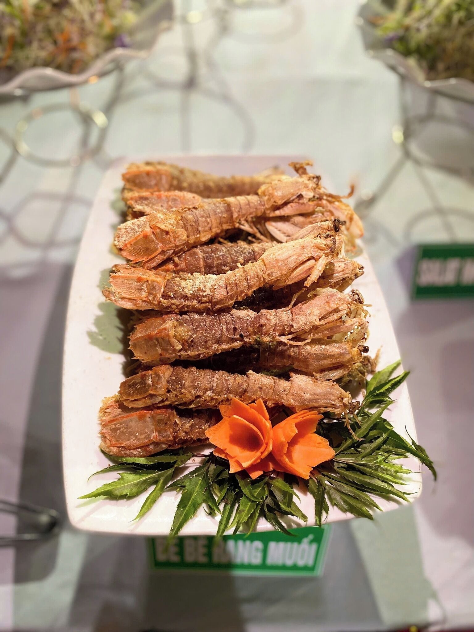 Un plato de insectos fritos adornado con hojas verdes y una flor naranja, con la etiqueta 'LE BEANG MUOI'.