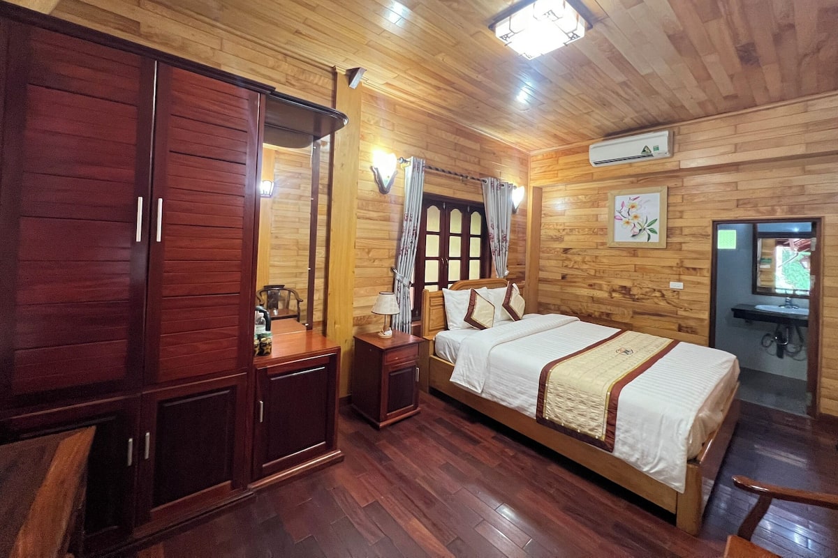 Een kamer met houten lambrisering, een bed, een garderobe en een kleine tafel met een lamp.
