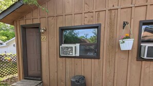 A wooden cabin with a door marked "22", a window with an air conditioning unit, and a black bag on the ground.